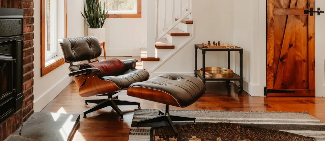 Eames-style lounge chair and ottoman beside a brick fireplace in a warm wood-trimmed room