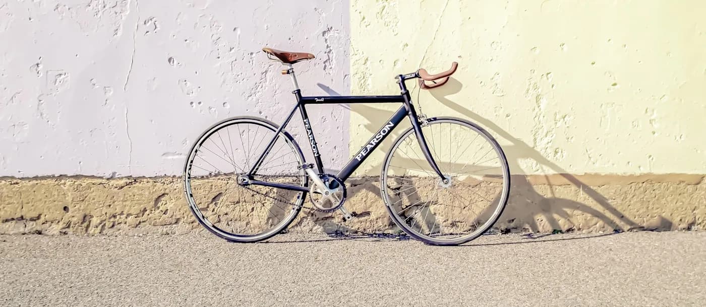 Black steel road bike with a brown leather saddle leaning against a sunlit wall